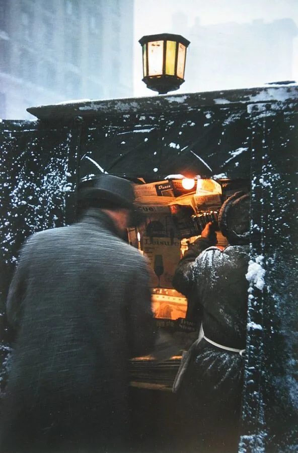 Photographie de rue par Saul Leiter montrant une scène hivernale avec deux hommes dans une cabine enneigée éclairée par une lanterne.